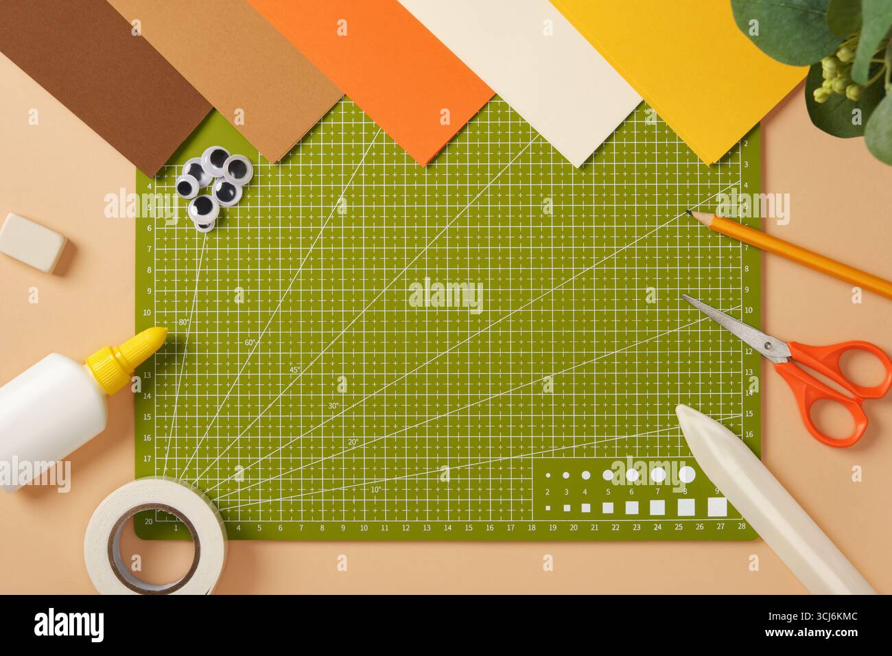 Grüne Schneidematte umgeben von farbigem Papier und Bastelwerkzeugen auf einem Tisch. Kreativer Arbeitsbereich für Kunst und Handwerk. Stockfoto