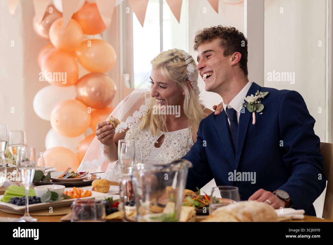 Braut und Bräutigam lachen zusammen am Tisch des Hochzeitsempfangs mit Essen und Getränken Stockfoto