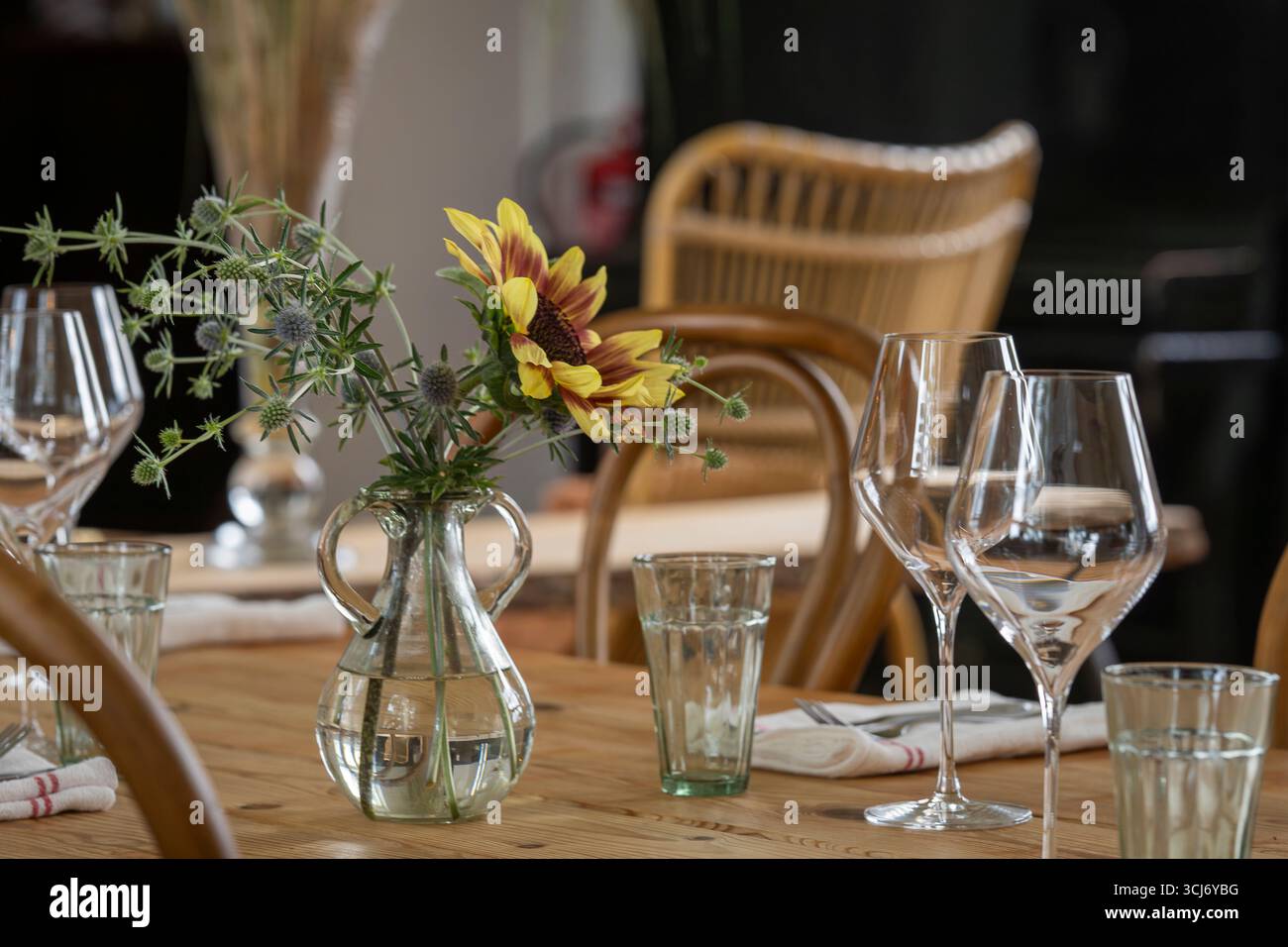 Holztisch für Gäste bereit. Holztisch mit Gläsern, Gabeln, Serviette. Eleganter Esstisch mit Sonnenblume (Helianthus annuus). Stockfoto