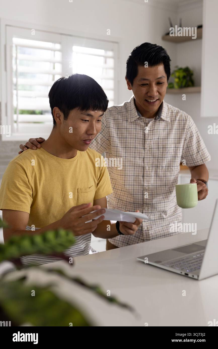 Vater und Sohn lächeln, während sie zu Hause zusammen einen Brief mit Laptop lesen Stockfoto