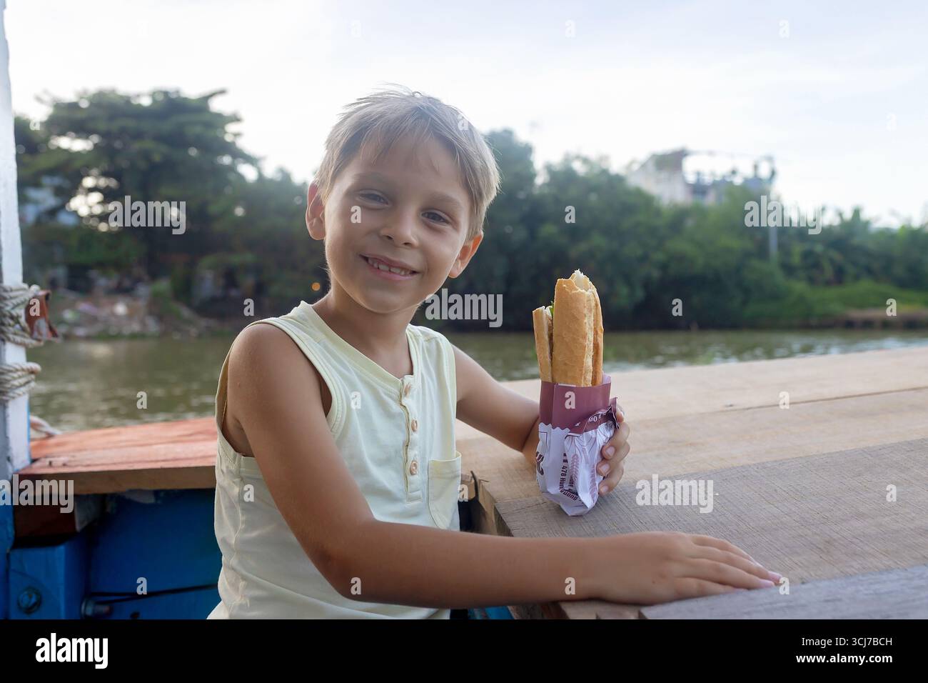 Kind, isst Sandwich auf einer Bootsfahrt in Vietnam, im Sommer Stockfoto