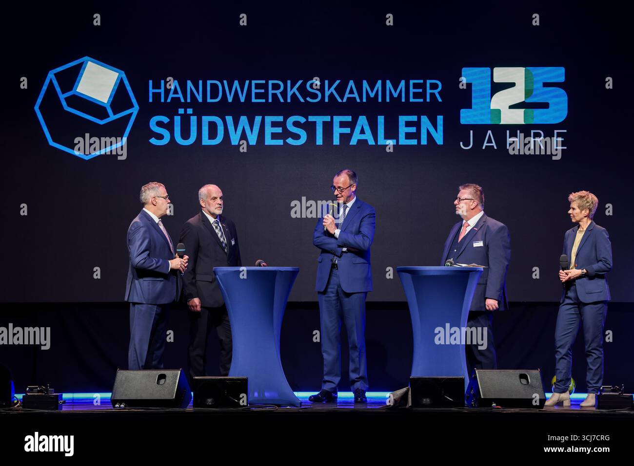Olsberg, Deutschland. September 2025. Jörg Dittrich (l-r), Präsident des Deutschen Handwerkbundes, Jochen Renfordt, Präsident der Handwerkskammer Südwestfalen, Bundeskanzler Friedrich Merz (CDU), Michael Neuhaus, Vizepräsident Mitarbeiter der Handwerkskammer Südwestfalen und Moderatorin Michaela Padberg stehen bei einer Podiumsdiskussion anlässlich des 125-jährigen Jubiläums der Handwerkskammer Südwestfalen auf der Bühne. Quelle: Christoph Reichwein/dpa/Alamy Live News Stockfoto