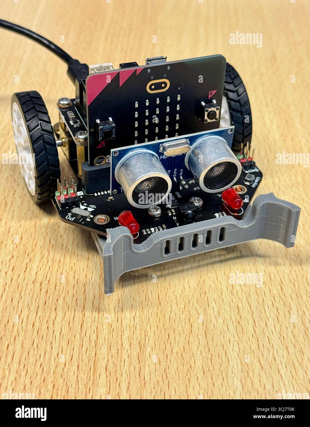 Kleiner Lehrroboter mit Mikro:Bit- und Ultraschallsensoren auf Holztisch. - Smartphone-aufgenommenes Stockfoto