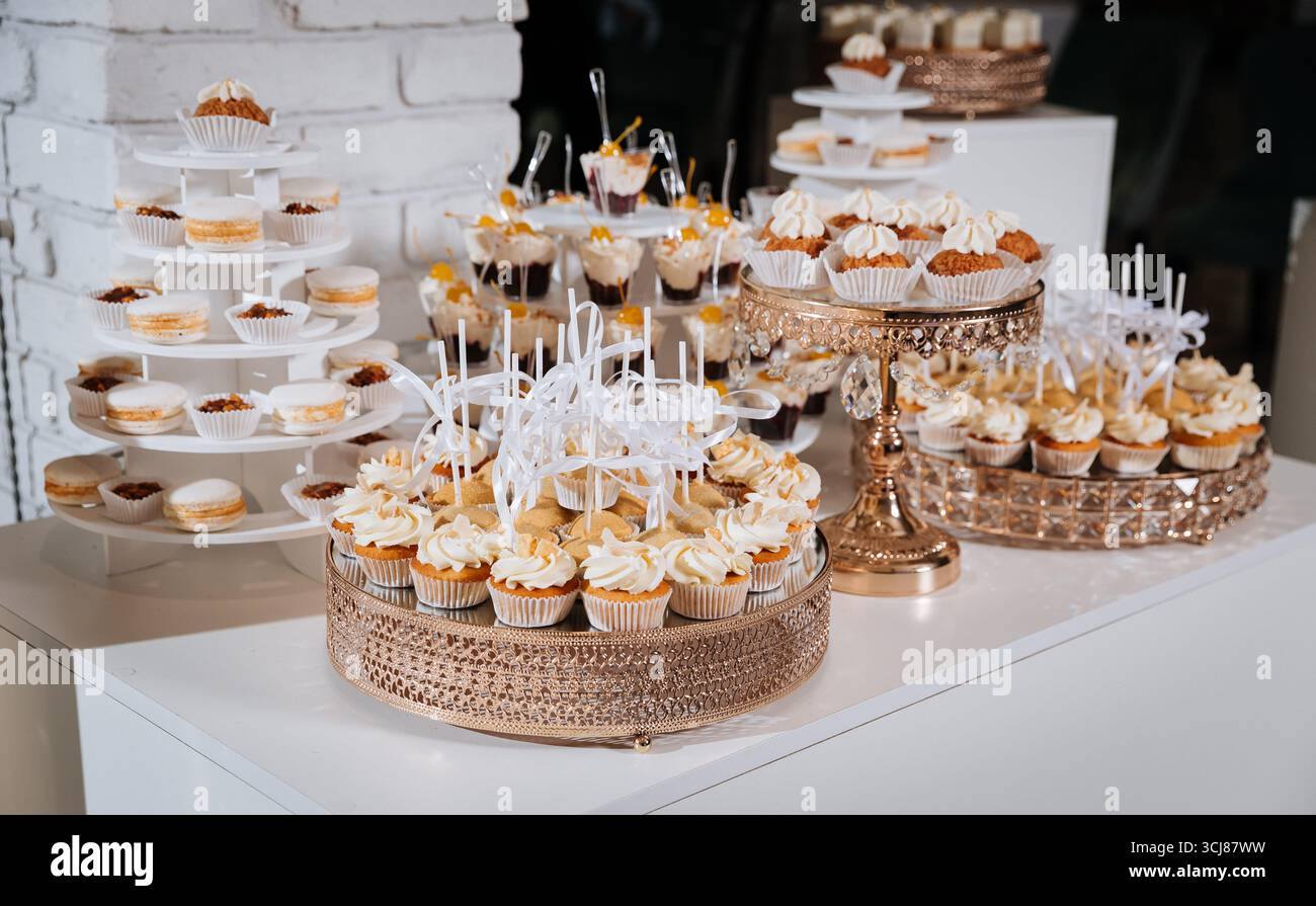Luxuriöse Schokoriegel mit Cupcakes, Macarons und Desserts auf eleganten goldenen Tabletts Stockfoto