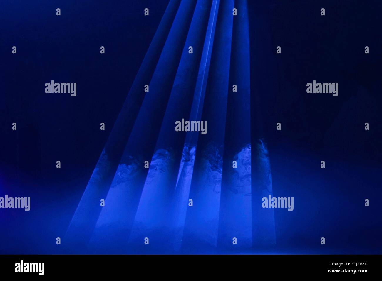 Geheimnisvolles blaues Licht enthüllt versteckte Figuren in einem dunklen Raum während einer fesselnden Performance Stockfoto