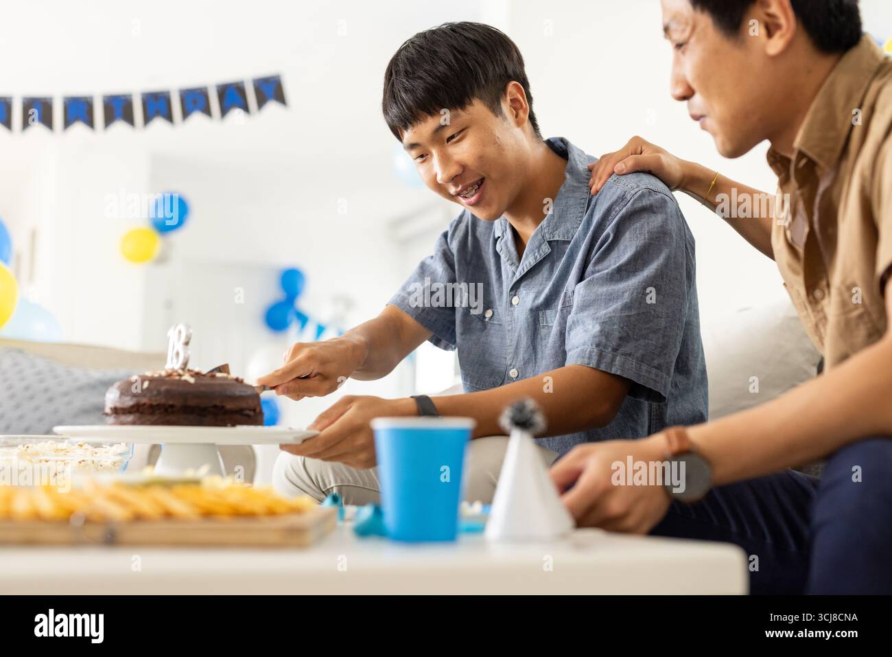 Vater und Sohn feiern zu Hause Geburtstag, schneiden Schokoladenkuchen zusammen Stockfoto