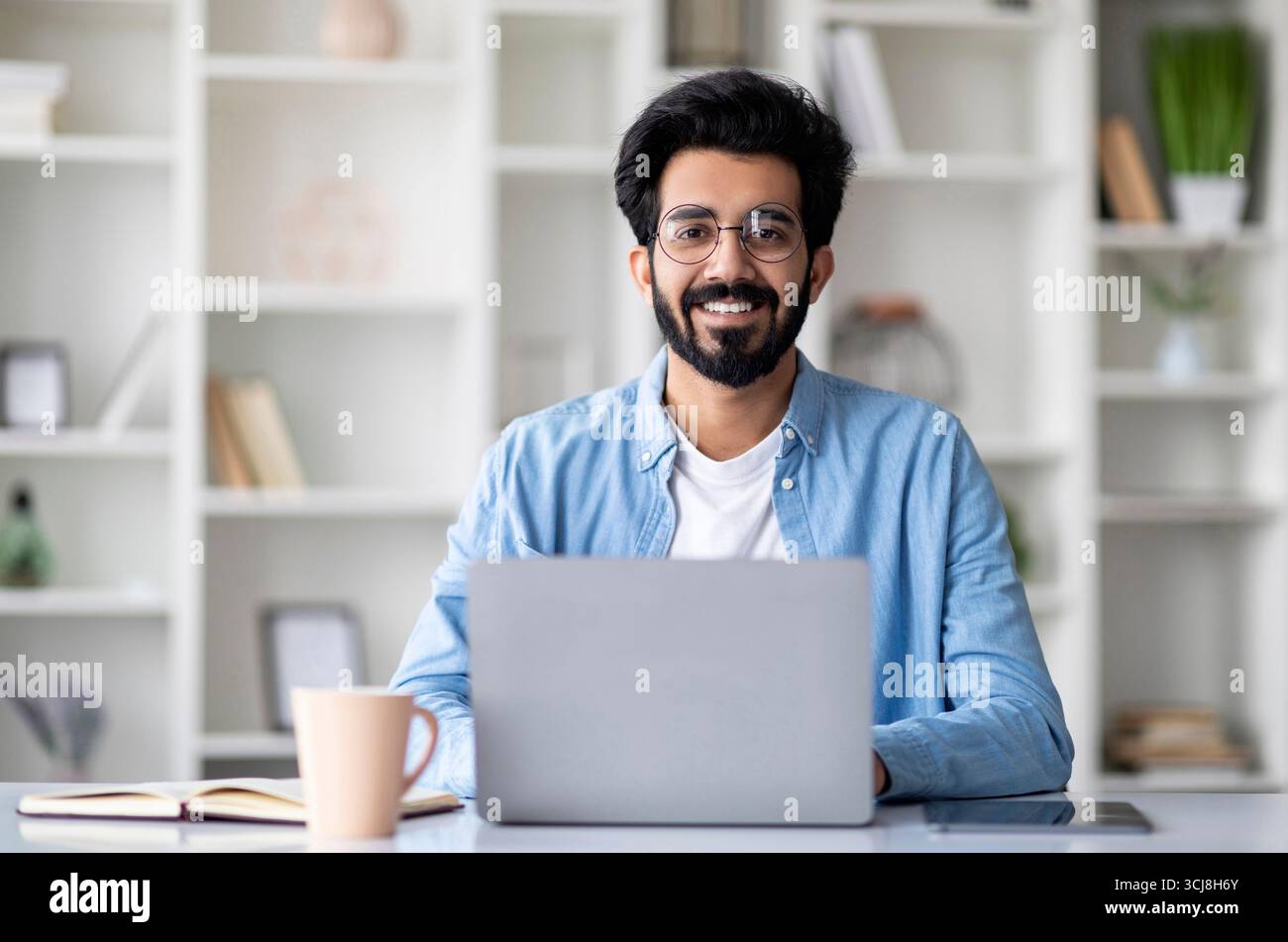 Attraktiver Junger Indischer Mann Sitzt Am Schreibtisch Mit Laptop Zu Hause Stockfoto