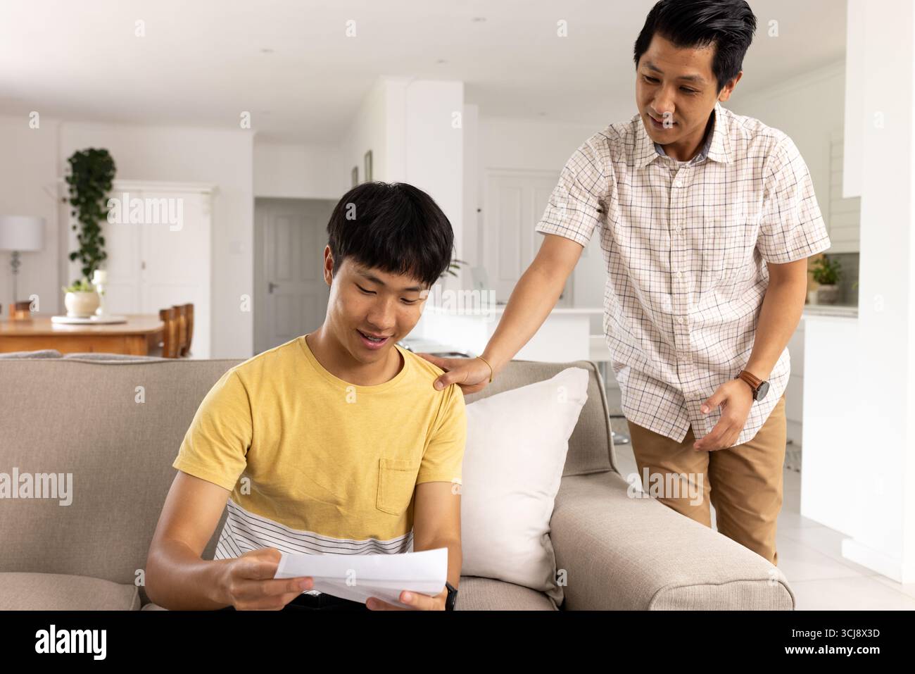 Vater ermutigt den Teenager-Sohn, den Brief zu Hause auf der Couch zu lesen und stolze Momente zu teilen Stockfoto