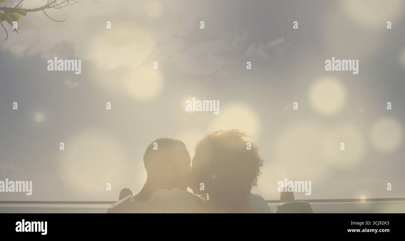 Sitzungspaar küsst sich am Geländer am Meer, beleuchtet von der Sonne mit Bokeh-Kugeln und schlanken Baumzweigen Stockfoto