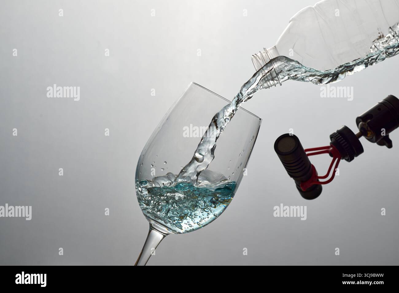 Ein Hochgeschwindigkeitsfoto von Süßwasser, das in ein Glas gegossen wird, das mit einem Mikrofon aufgenommen wurde. Ein vielseitiges Konzept für ASMR, Hydration, Reinheit und Umgebung Stockfoto