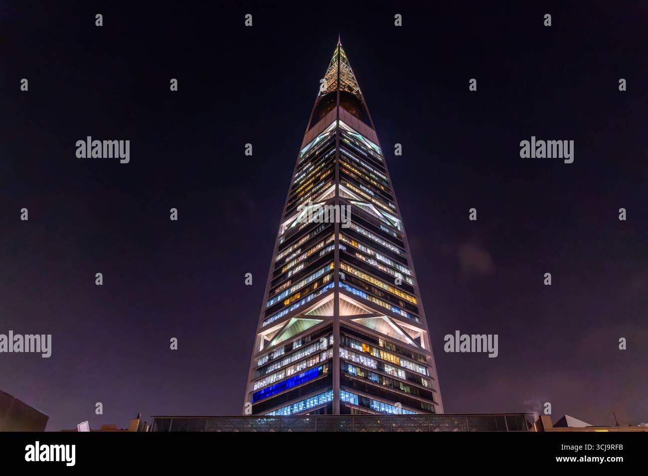 Der nächtliche Blick auf den Al Faisaliah Tower in Riad, Saudi-Arabien, erhebt sich mit seiner unverwechselbaren goldenen Kugel in der Nähe des Gipfels, umgeben von Palmen Stockfoto