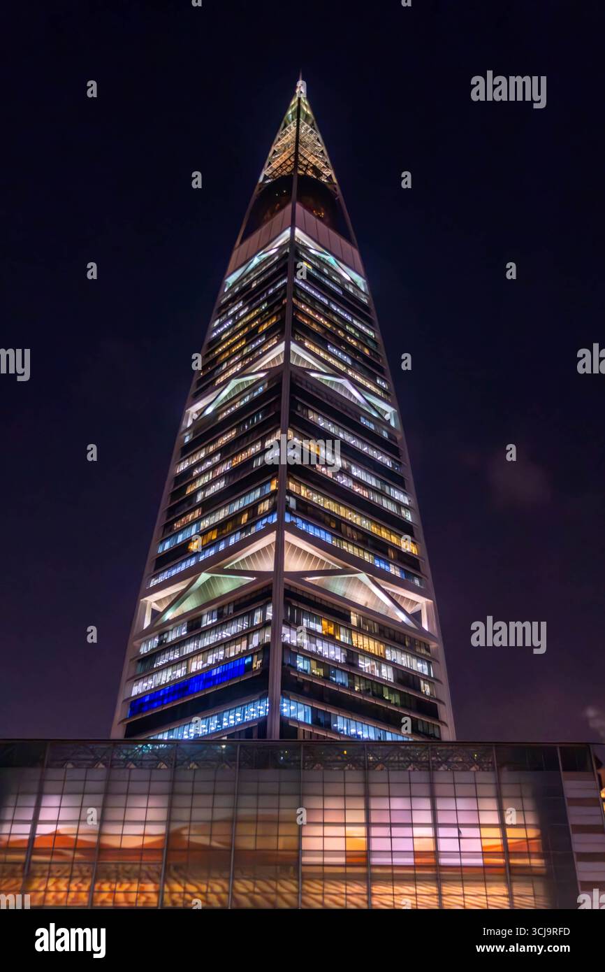 Der nächtliche Blick auf den Al Faisaliah Tower in Riad, Saudi-Arabien, erhebt sich mit seiner unverwechselbaren goldenen Kugel in der Nähe des Gipfels, umgeben von Palmen Stockfoto