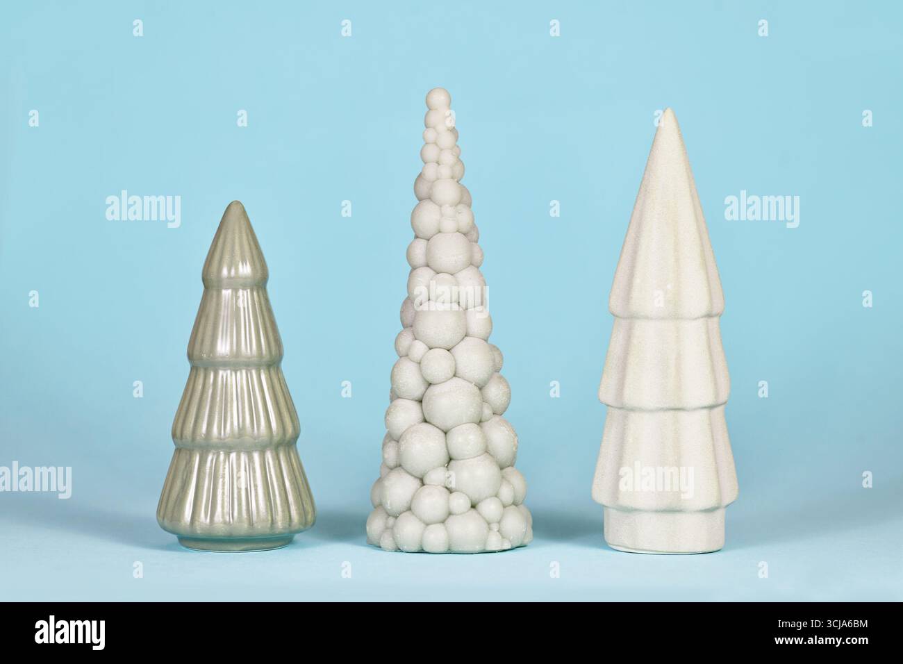 Drei unterschiedlich geformte hellgrüne Keramik-Weihnachtsbäume auf blauem Hintergrund Stockfoto
