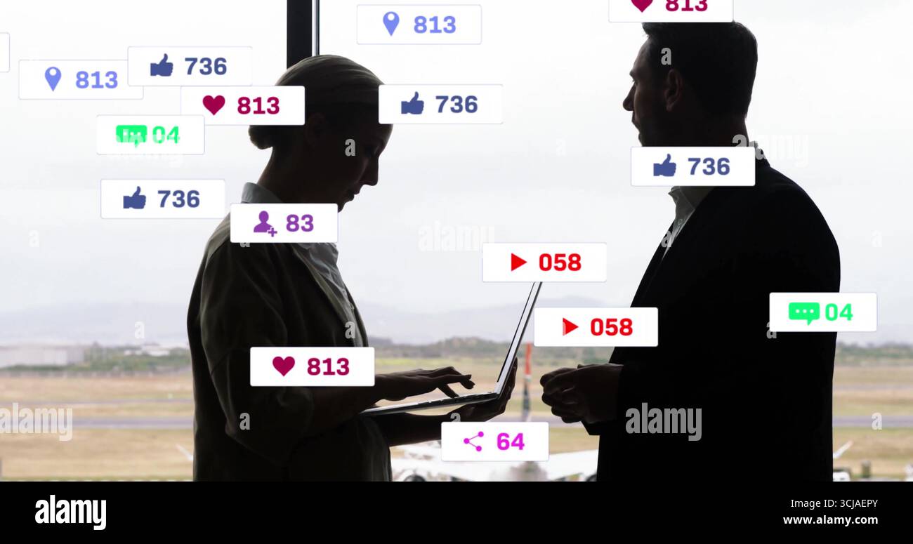 Stehende Kollegen, die einen Laptop schreiben und das Smartphone am Flughafenfenster halten, mit Symbolen in sozialen Medien Stockfoto