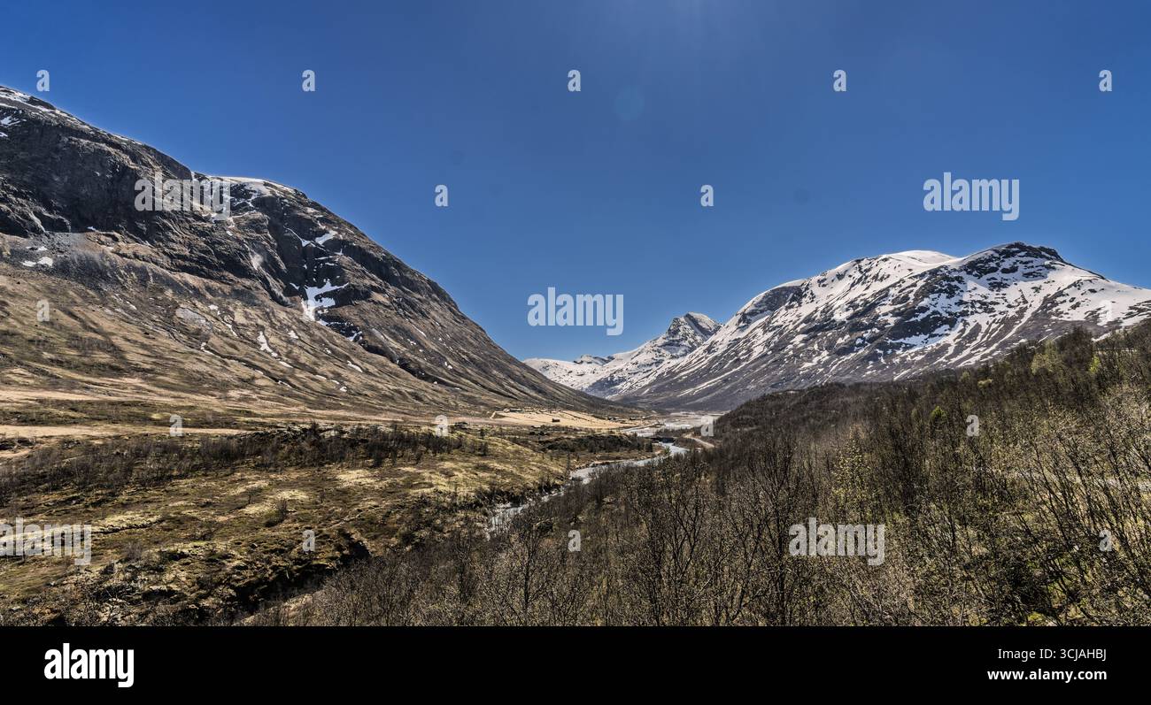 Majestätische Landschaft mit einem ruhigen Tal, flankiert von schneebedeckten Bergen und einem sich windenden Fluss, alles unter einem klaren blauen Himmel, der Ruhe und Natu weckt Stockfoto