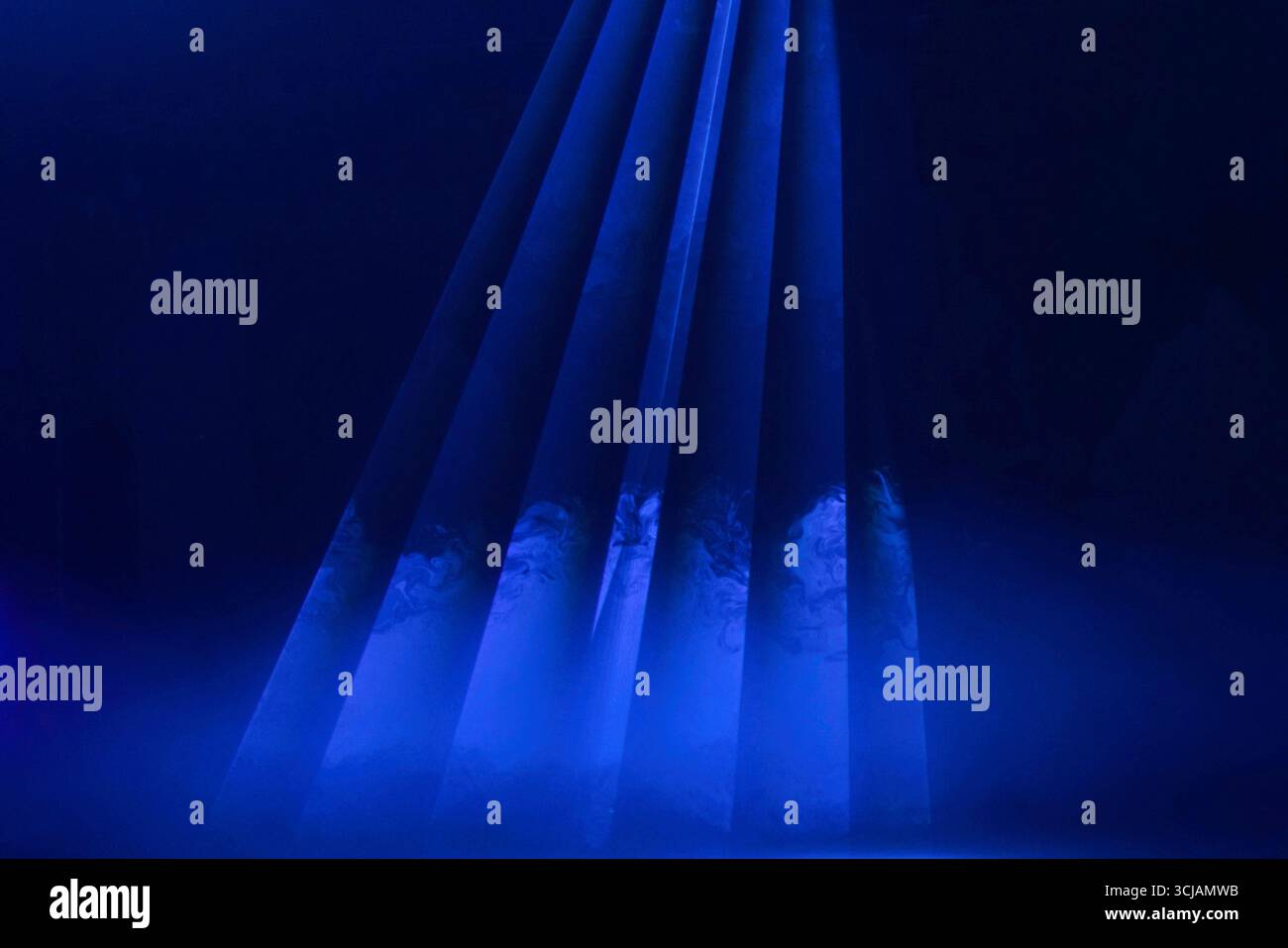 Geheimnisvolles blaues Licht enthüllt versteckte Figuren in einem dunklen Raum während einer fesselnden Performance Stockfoto