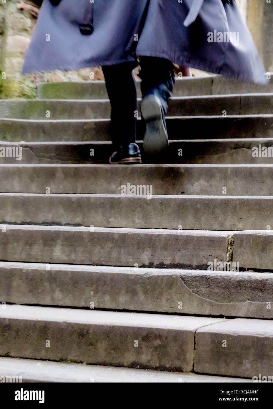Eine Person läuft eine Steintreppe hinauf, trägt einen langen Mantel. Stockfoto