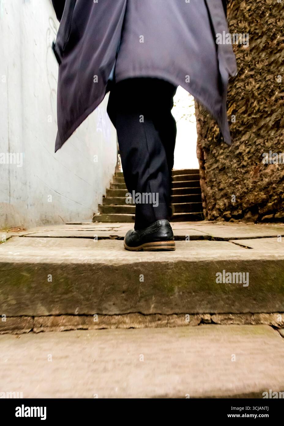 Eine Person in dunklem Mantel und Hose geht eine Treppe hinauf. Stockfoto
