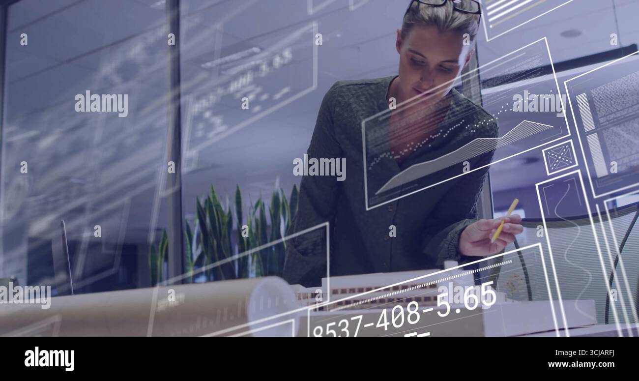 Der Architekt in Bluse, der sich über das Modell im modernen Atelier lehnt, mit Monitoren, die Code anzeigen Stockfoto