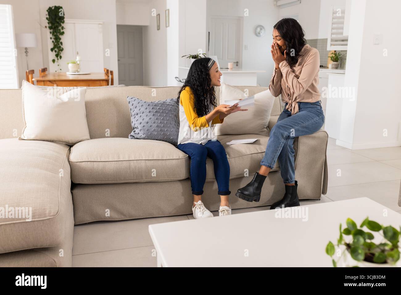 Mutter und Tochter teilen zu Hause spannende Neuigkeiten, beide sehen fröhlich und überrascht aus Stockfoto