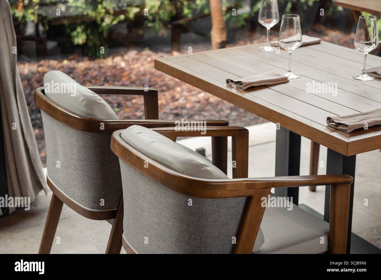 Leerer Tisch und Stühle in einem Restaurant. Terrasse mit Holzstühlen und Tisch, Büsche im Garten im Hintergrund. Stockfoto