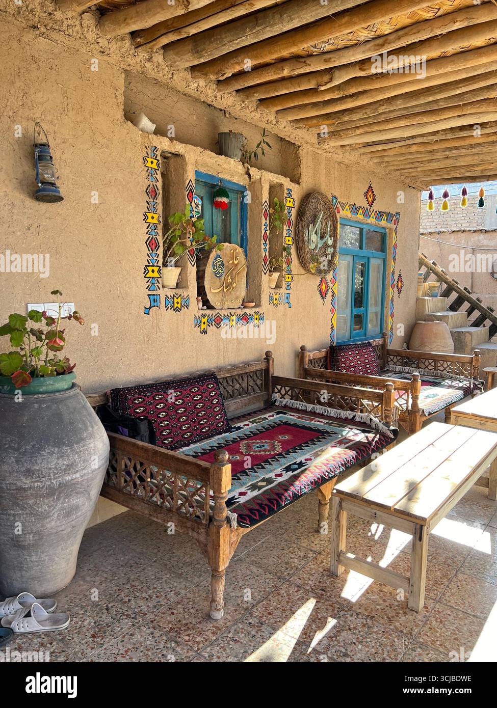 Farbenfrohe persische Teppiche und Holzbänke schmücken die Veranda eines traditionellen Gästehauses im Südiranischen. Stockfoto Farbenfrohe persische Teppiche und Holzbänke schmücken die Veranda eines traditionellen Gästehauses im Südiranischen. Stockfoto