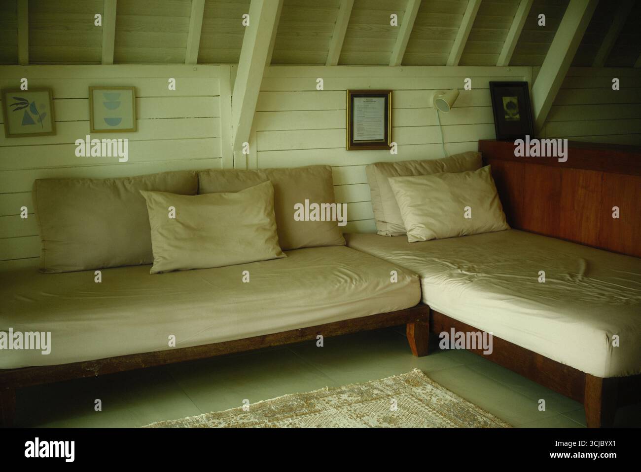 Tabanan, Bali, Indonesien – 26. August 2025: Minimalistisches L-förmiges Holzsofa mit beigefarbenen Kissen in einer gemütlichen Wohnecke Stockfoto