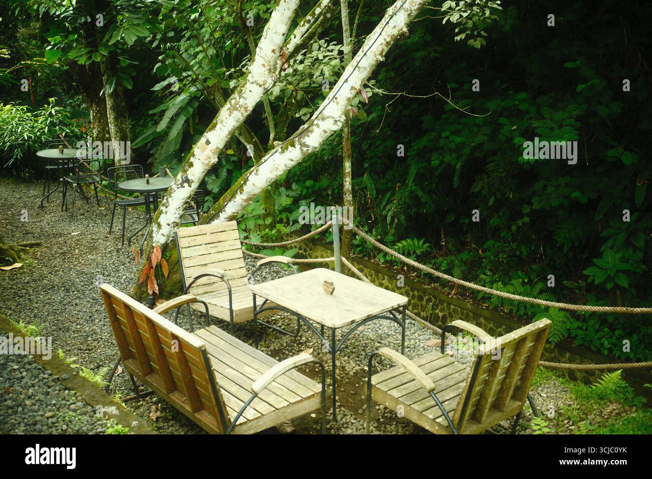 Ein gemütliches rustikales Gartenmöbel auf einem Kiesweg in einem Waldcafé Stockfoto