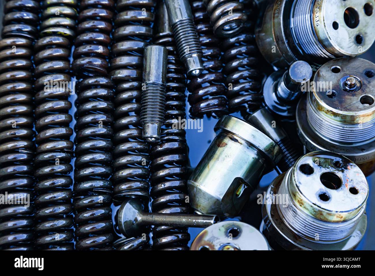 Mechanische Stahlteile mit Maschinenöl geschmiert, Nahaufnahme. Stahleinspritzdüsen, Federn, Buchsen, Bolzen und Gewindeteile in Öl. Stockfoto