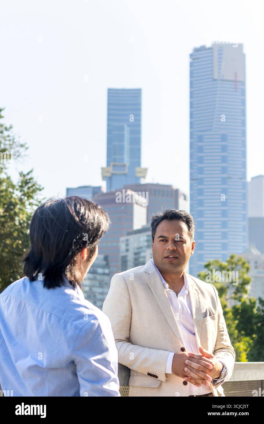 Zwei professionelle Männer führen ein Geschäftsgespräch mit der legendären Skyline von Melbourne im Hintergrund, die das urbane professionelle Umfeld unterstreicht Stockfoto