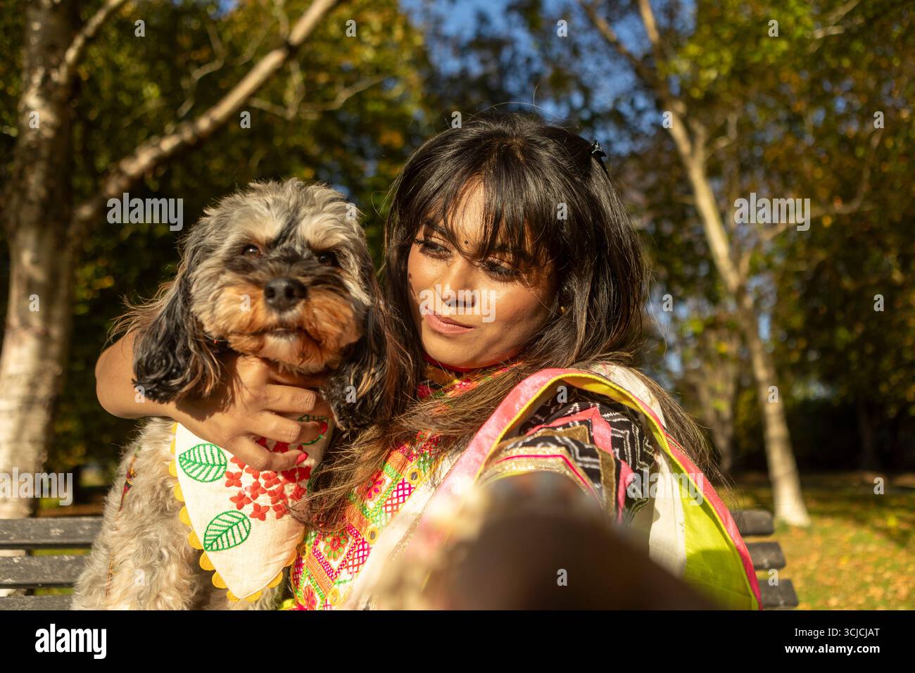 Eine fröhliche Indianerin umarmt ihren Hund im Park und hält an einem sonnigen Tag einen herzerwärmenden Moment der Gemeinschaft und der Schönheit der Natur fest Stockfoto