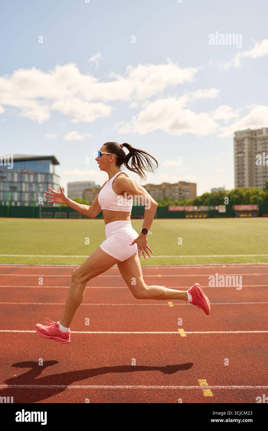 Energiegeladene Frau, die bei hellem Sonnenlicht auf einer Outdoor-Strecke läuft und Sportlichkeit und einen aktiven Lebensstil zum Ausdruck bringt. Das Bild hebt ihren Fokus und ihren Det hervor Stockfoto