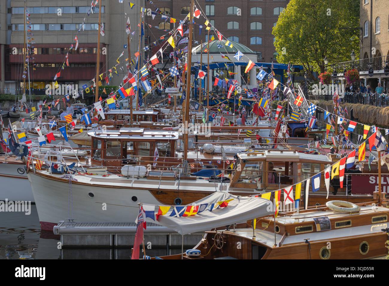 London, Großbritannien. September 2025. Eine festliche Yachthafenszene mit Vintage-Holzbooten, die mit farbenfrohen Signalflaggen verziert sind. Die Hafenanlage ist lebhaft mit Besuchern, mehrstöckigen Gebäuden und Bäumen im Hintergrund, was auf ein öffentliches maritimes Kulturerbe hindeutet. St. Katharine Docks Classic Boat Festival mit über 60 klassischen und alten Booten, darunter kleine Schiffe aus Dunkirk, die der Öffentlichkeit präsentiert werden. Penelope Barritt/Alamy Live News Stockfoto
