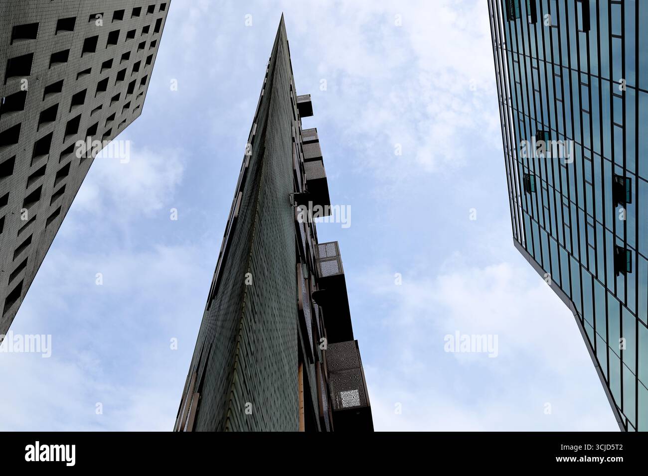 Flacher Blick auf einen schlanken Turm mit Balkonen am IJDock, Amsterdam, Niederlande, zwischen Glas- und Backsteinbüroblöcken unter einer hellen Wolke. Stockfoto