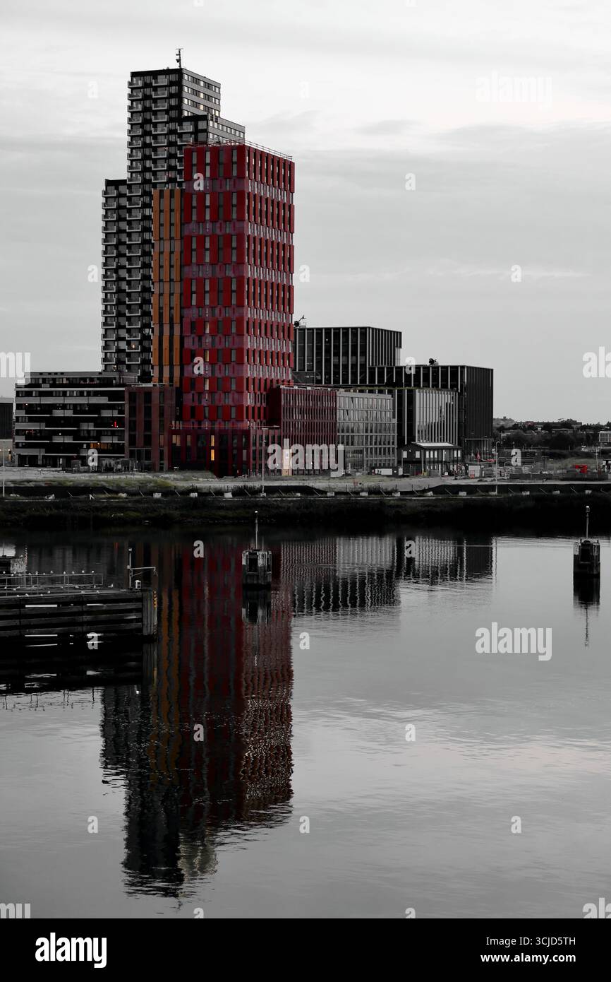 Der Justus-Turm in Sluisbuurt mit dem Hogeschool Inholland Campus spiegelt sich bei Sonnenuntergang im Wasser, über den Hafen in Amsterdam, Niederlande. Stockfoto