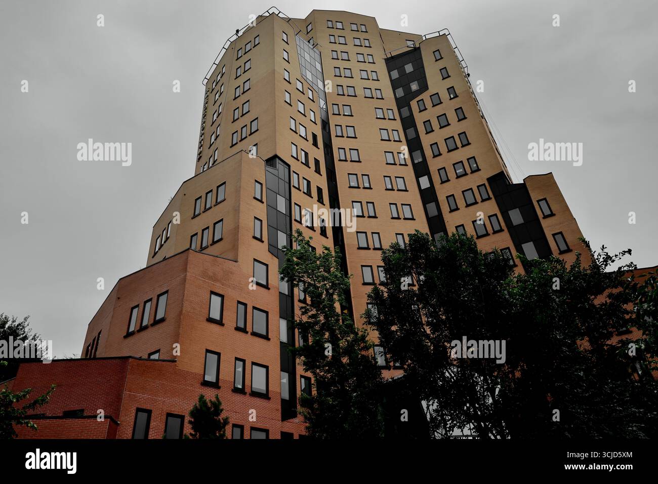 Tiefwinkelansicht der Teleport Towers, Sloterdijk, Amsterdam, Niederlande, mit Regus Büros, Stufenziegel und dunkle Verkleidung, Bäume im ruhigen Vordergrund. Stockfoto