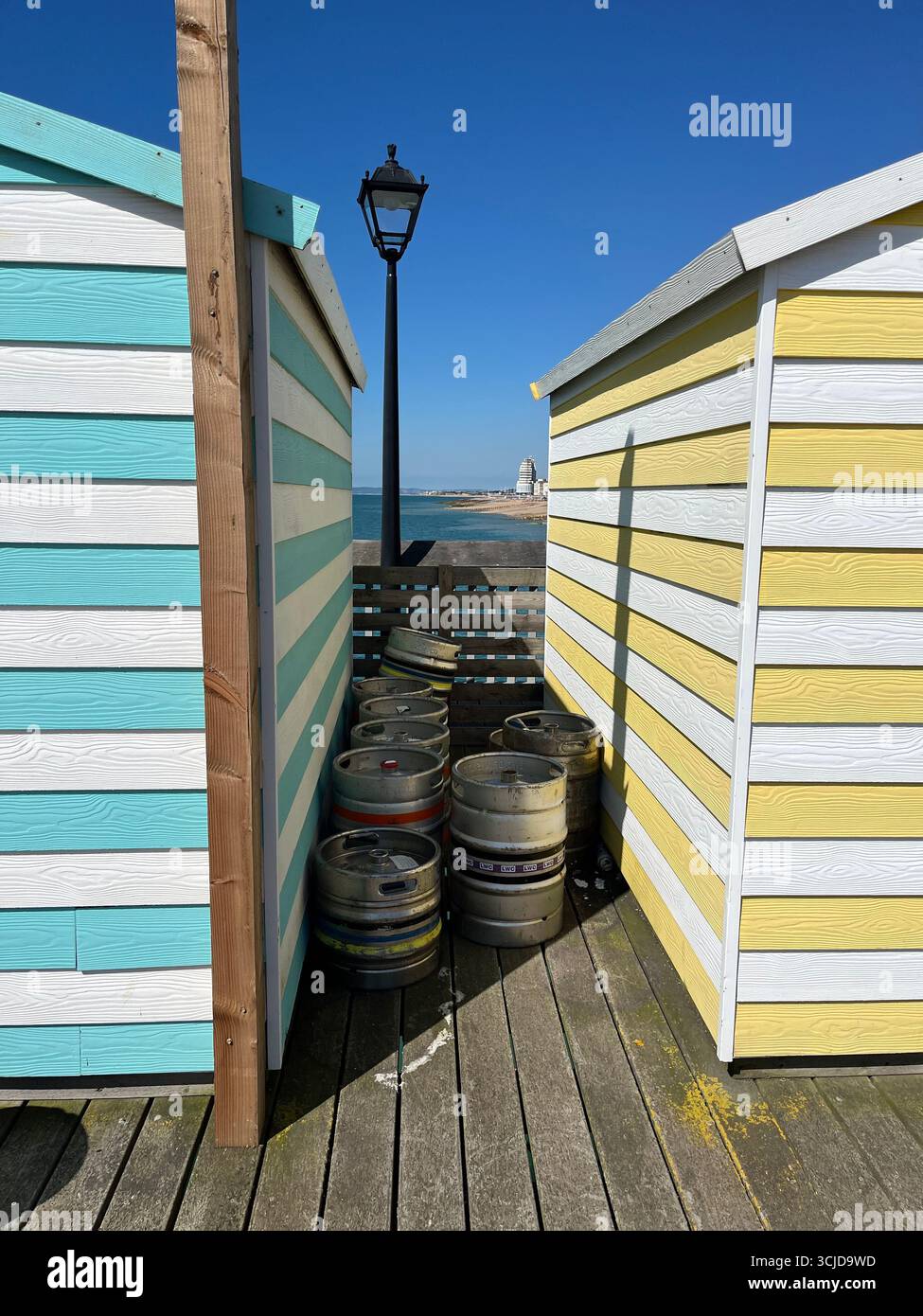 Farbenfrohe gestreifte Hastings Pier Hütten mit Bierfässern und alter Lampe, klarer blauer Himmel - Smartphone-aufgenommenes Stockfoto