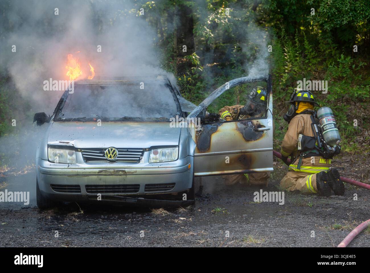 Feuerwehrleute bekämpfen ein brennendes Autofeuer mit starkem Rauch und Flammen und zeigen Notfallmaßnahmen, Brandschutz und dramatische Rettungsaktionen. Stockfoto