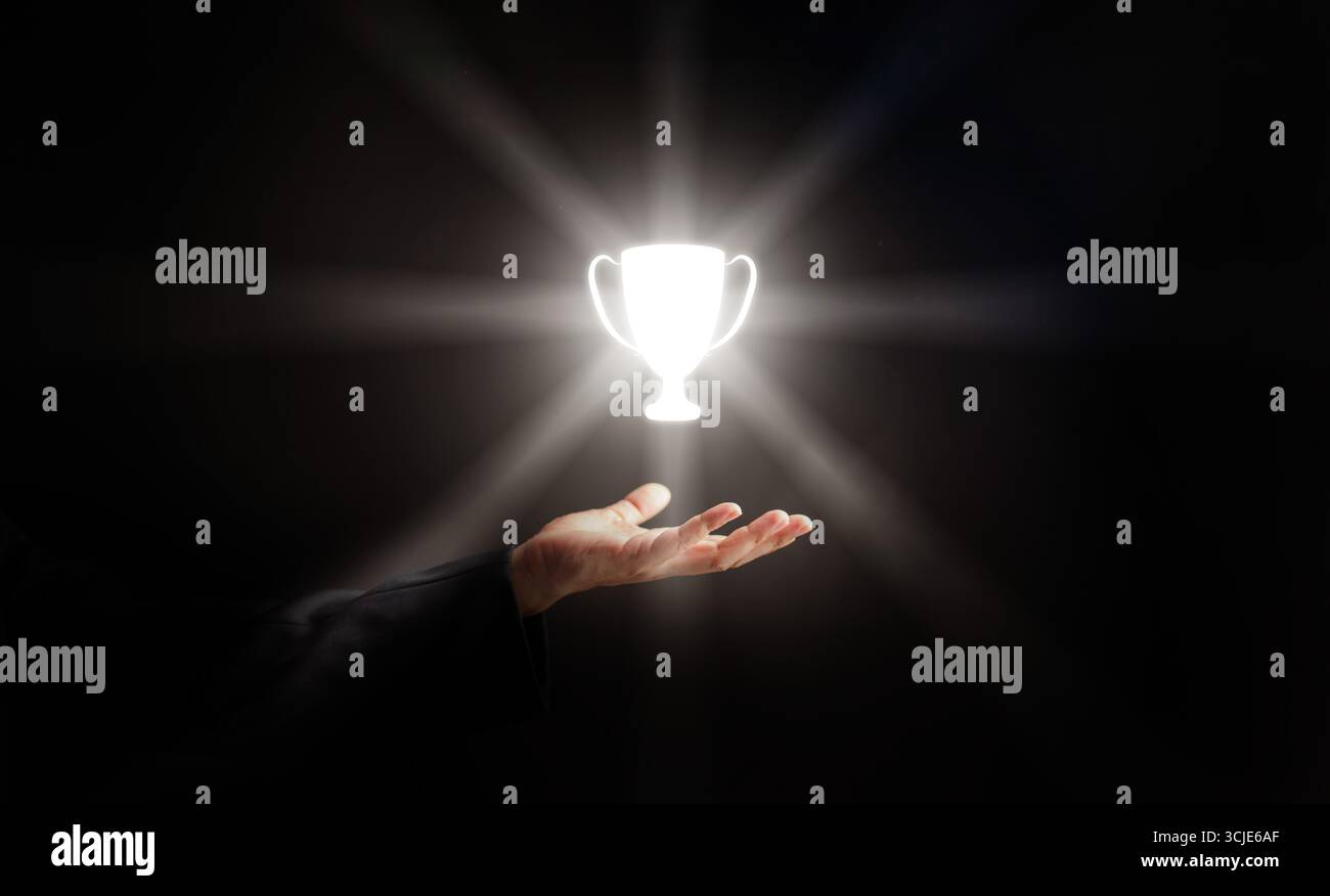 Glühende Trophäe, die über der Hand eines Geschäftsmannes schwingt und Erfolg, Leistung, Führung und Business Excellence auf schwarzem Hintergrund symbolisiert. Perfekt Stockfoto