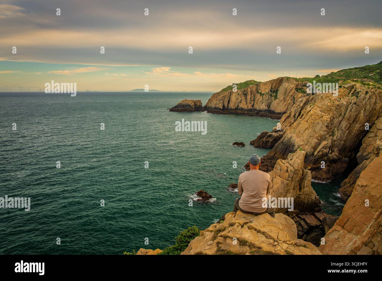 Mann allein, der auf der Klippe sitzt, genießt die Aussicht Stockfoto
