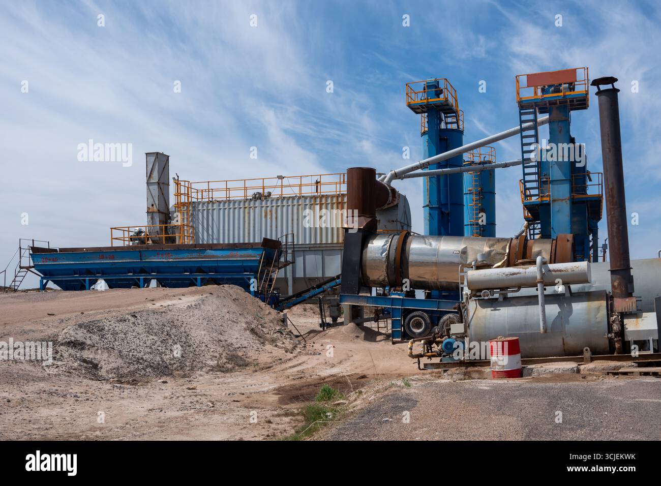 Große industrielle Asphaltmischanlage mit blauen Maschinen und Förderern, erfasst an einem sonnigen Tag mit Himmelshintergrund, repräsentiert Bauarbeiten Stockfoto