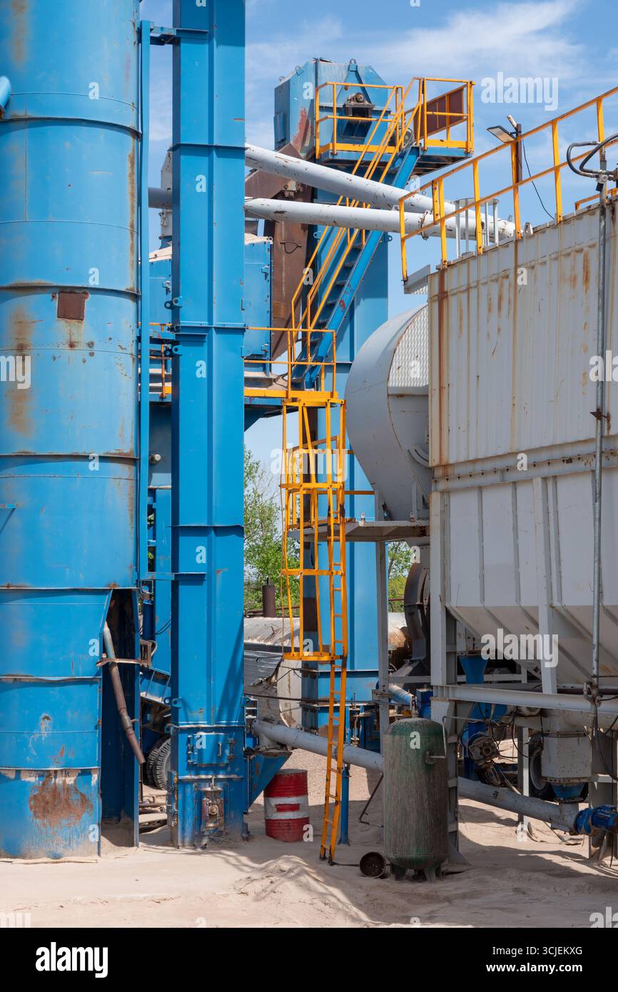 Große blaue Industrieausrüstung mit gelben Sicherheitsleitern und Rohren auf einer Baustelle, erfasst unter einem sonnigen Himmel mit natürlichem Hintergrund Stockfoto