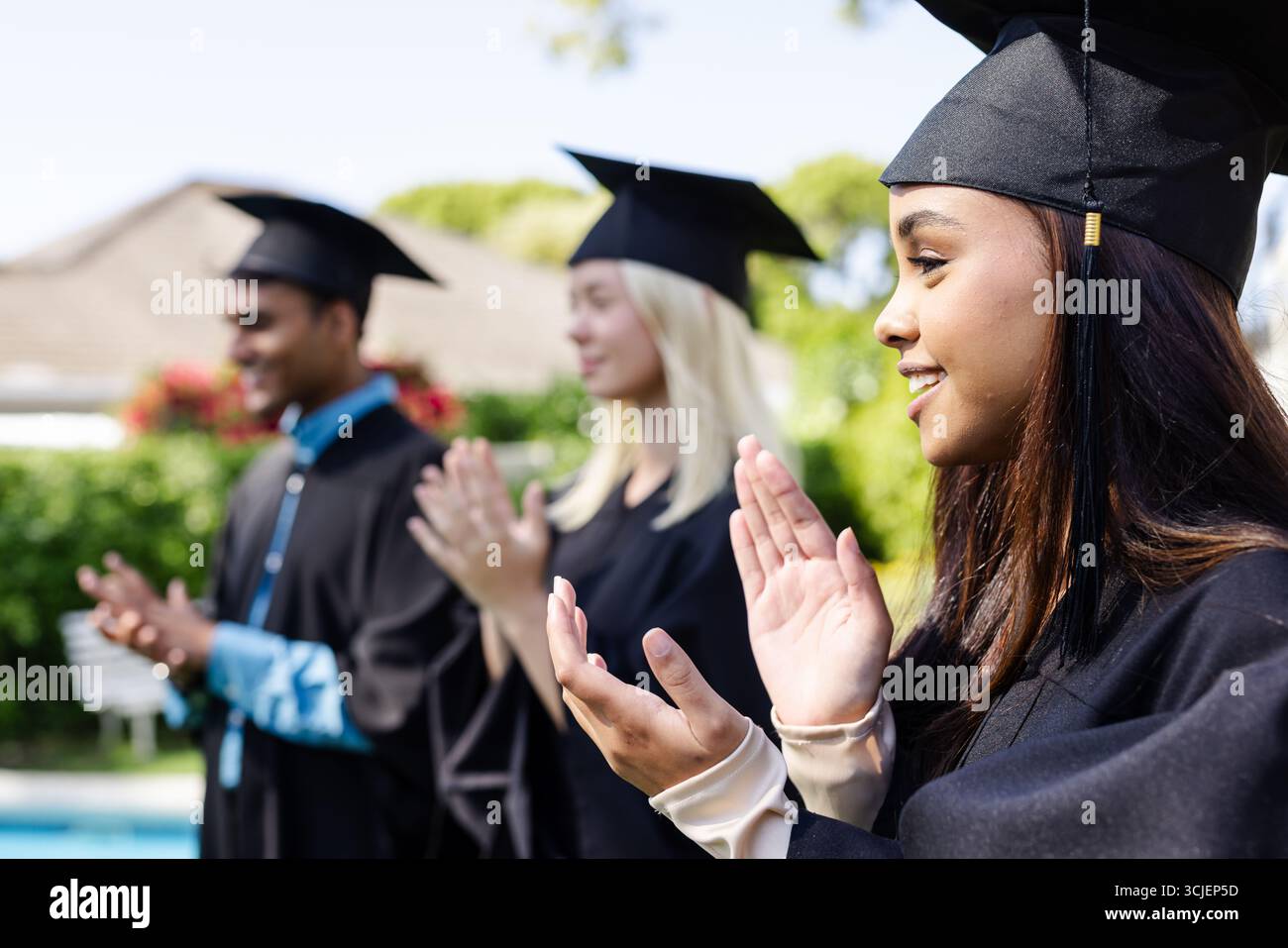 Absolventen in Mützen und Kleidern klatschen im Freien, um akademische Leistungen zu feiern Stockfoto