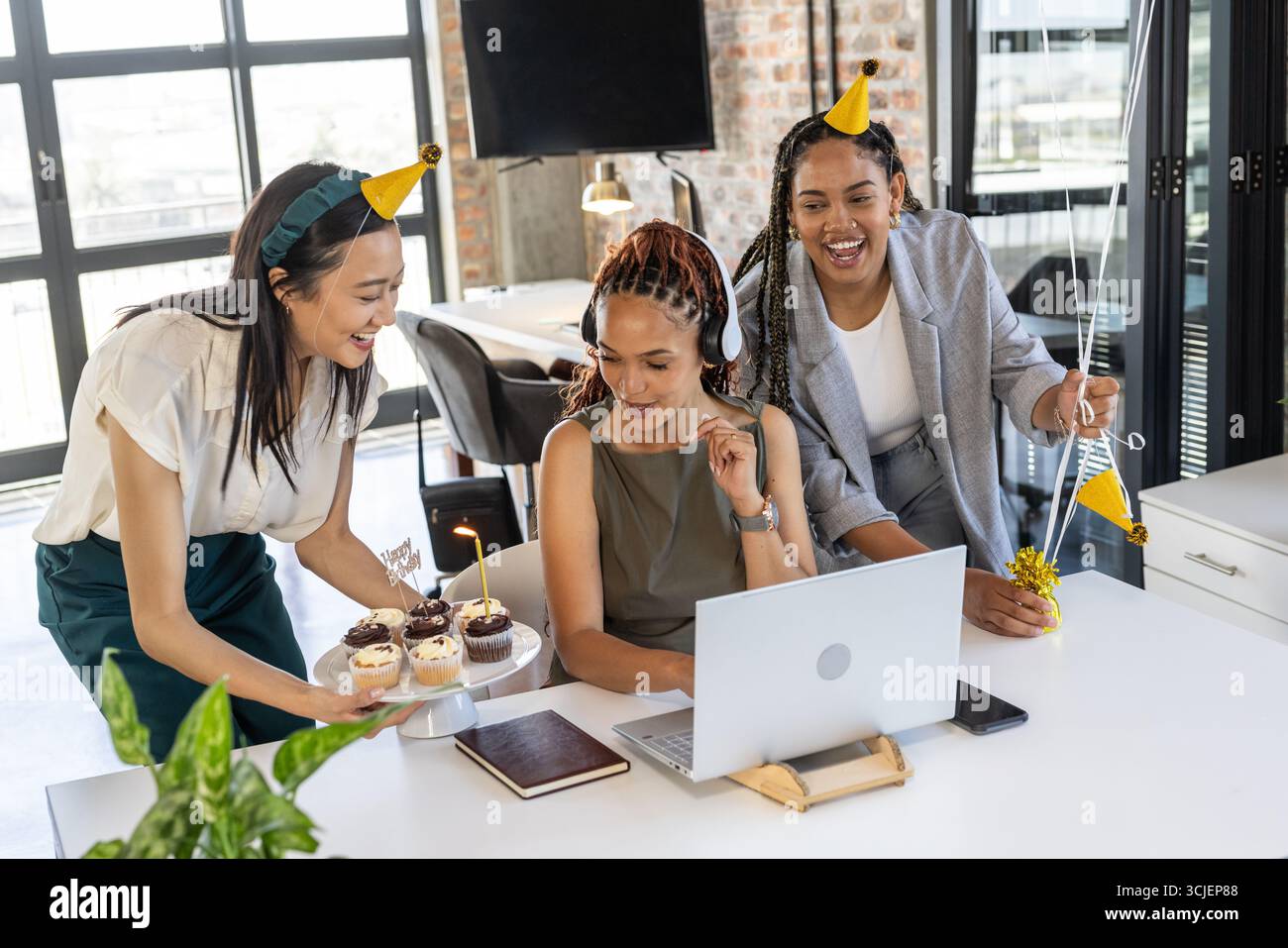 Kollegen, die im Büro mit Cupcakes und Partyhüten feiern, genießen Erfolg Stockfoto