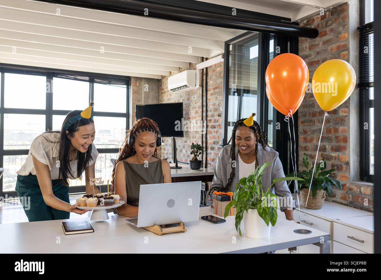 Geburtstag im Büro mit Cupcakes und Ballons feiern, Kollegen lächeln zusammen Stockfoto