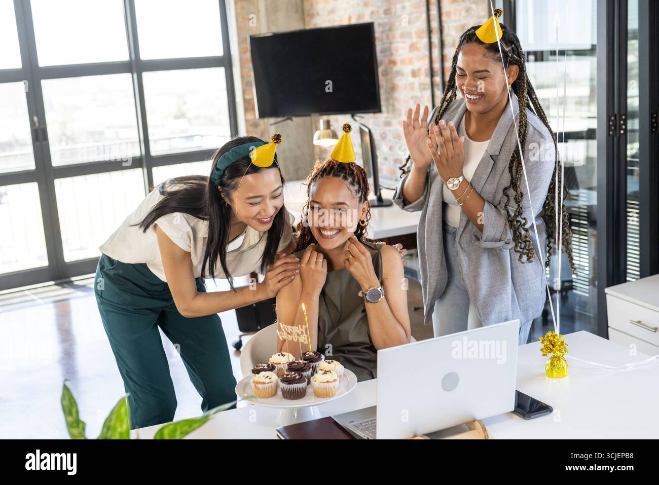 Wir feiern Geburtstag im Büro, Kollegen tragen Partyhüte und teilen fröhlich Cupcakes Stockfoto