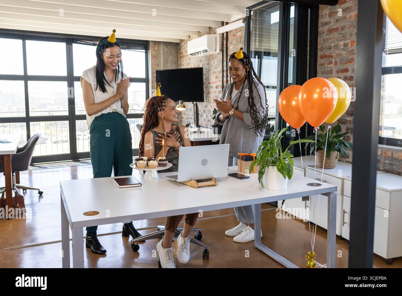 Wir feiern Geburtstag, Kollegen im Büro tragen Partyhüte, teilen Cupcakes glücklich Stockfoto