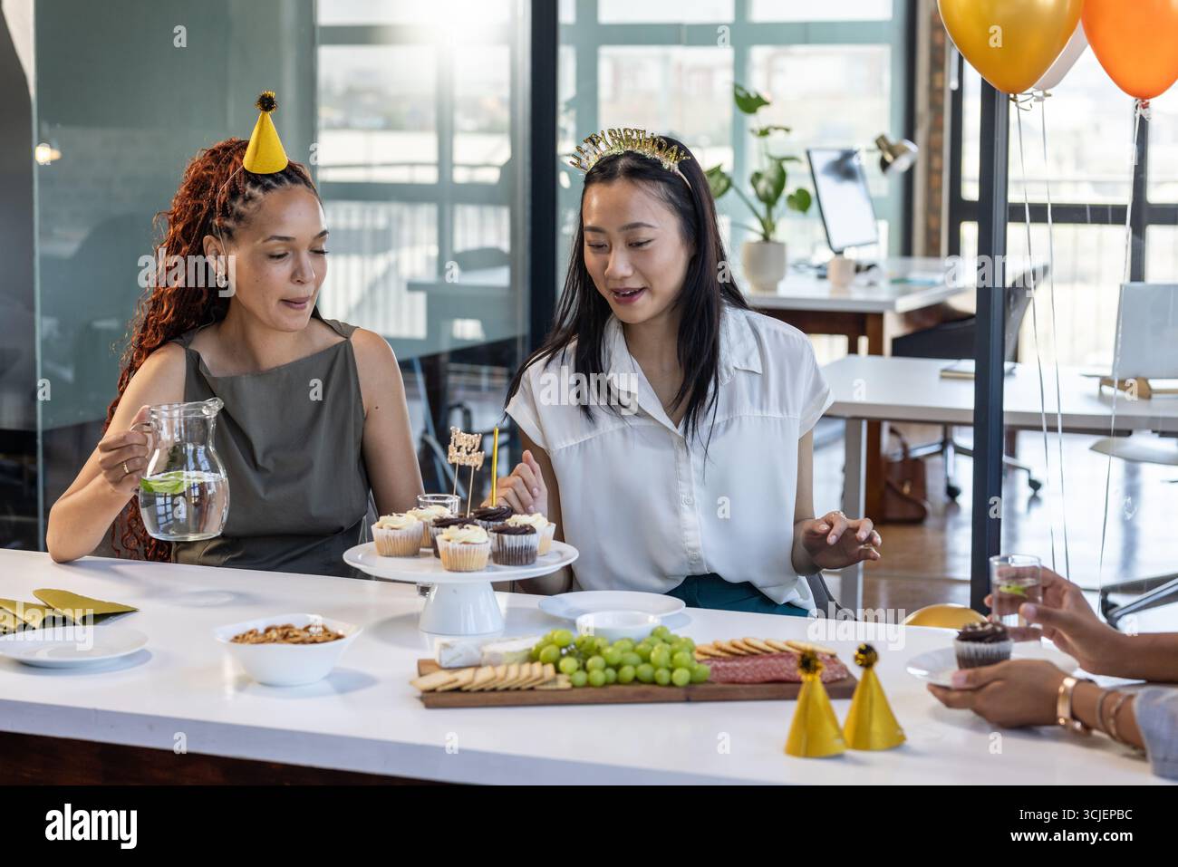 Feiert Geburtstag im Büro, Kollegen mit Cupcakes und Partyhüten zusammen Stockfoto