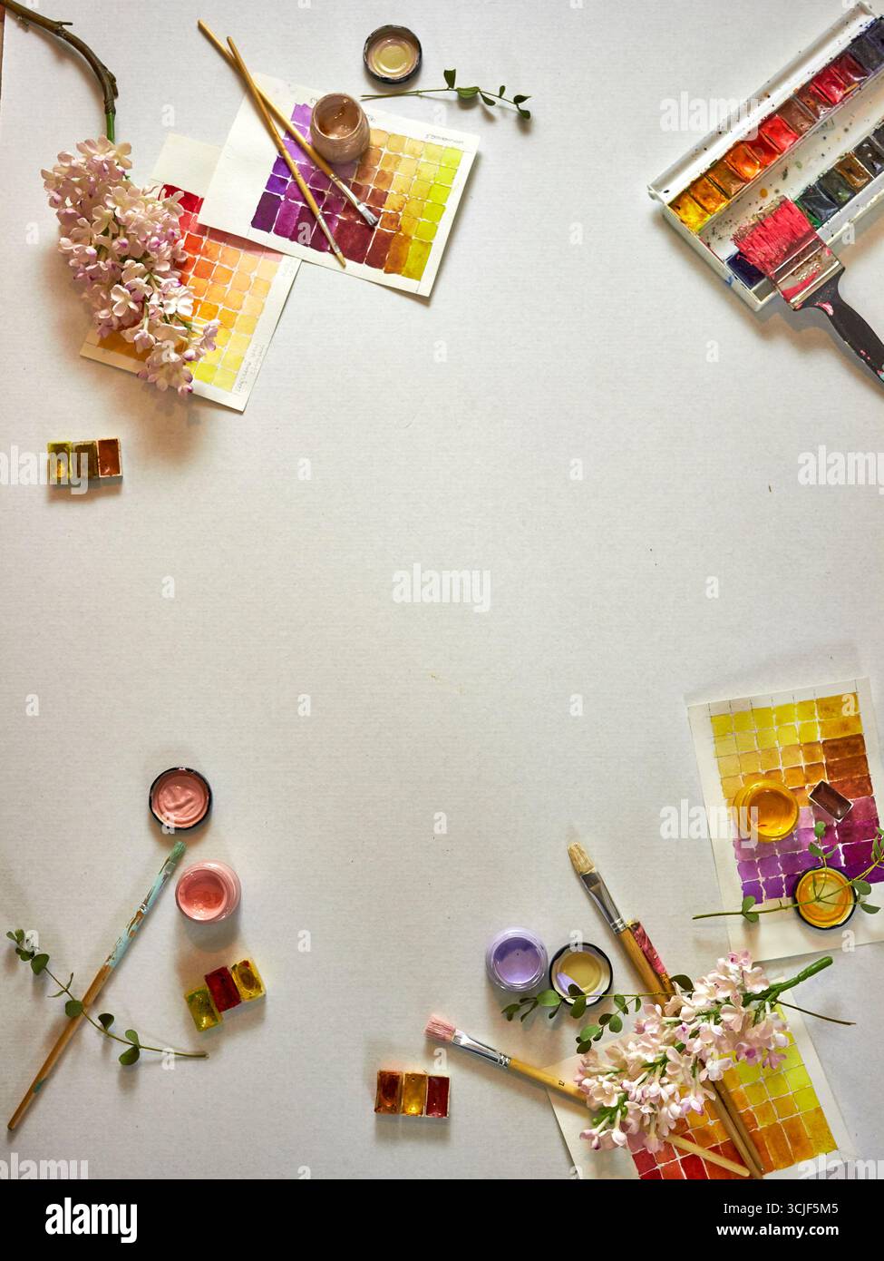 Flach mit Aquarellfarben, Pinseln, Farbmustern und frischen Blumen auf hellem Hintergrund. Künstlerischer Arbeitsbereich mit kreativen Werkzeugen und leerem SP Stockfoto