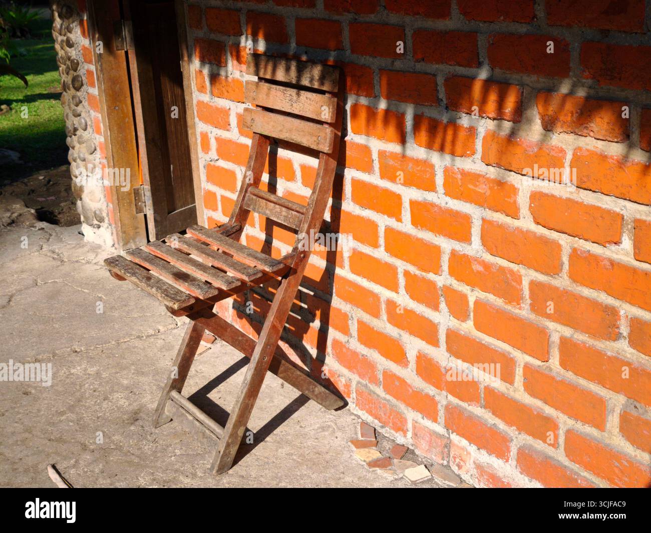 Ein abgenutzter Holzstuhl lehnte sich an eine orangene Ziegelwand Stockfoto